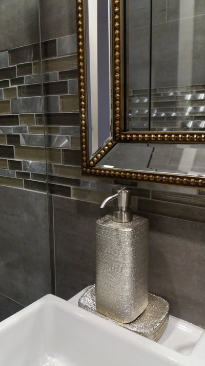 Bathroom mirror in silver and gold frame with matching bathroom accessories on feature tiles.