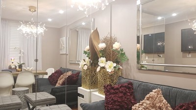 Living room looks bigger with mirrored wardrobes. Cushions and a floral arrangement add colour and style.